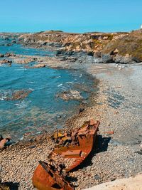 Damaged rock on beach against clear blue sky