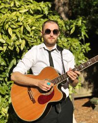 Portrait of man playing guitar against plants