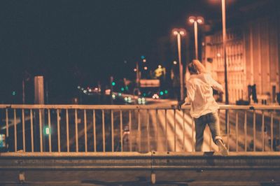 Rear view of woman walking on illuminated bridge at night