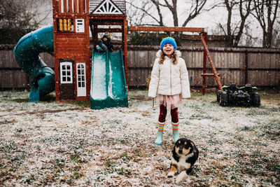 Two young kids and puppy playing in backyard on snowy day