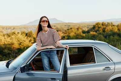 Portrait of young woman sitting on car