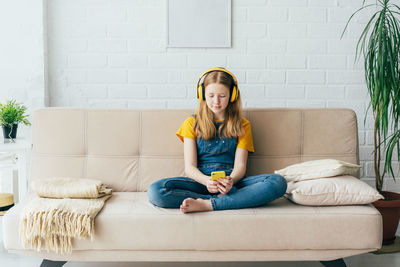 Full length of girl listening musing sitting on sofa at home