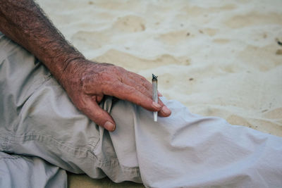 Midsection of man holding weed joint while sitting on beach