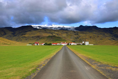 Empty road amidst field against sky