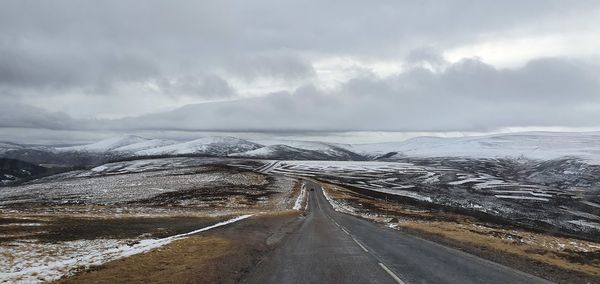 Empty road leading towards snowcapped mountains against sky