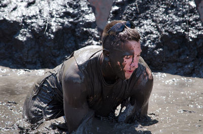 Mud covered athlete crawls through a muddy river during a race