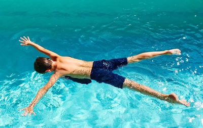 Rear view of shirtless boy with rams raised swimming in pool during sunny day