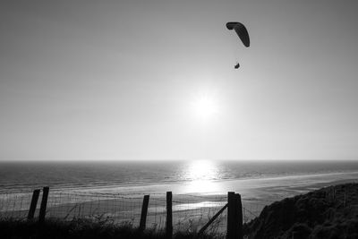 Silhouette person paragliding above sea during sunny day