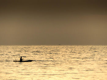 Silhouette person in sea against sky during sunset