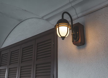 Low angle view of illuminated light bulb hanging on wall of building