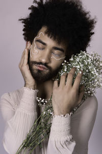 Genderblend man with make-up holding flowers