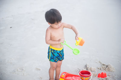 Shirtless boy playing with toys at beach