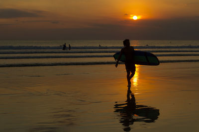 Silhouette man with surfboard walking on shore at beach