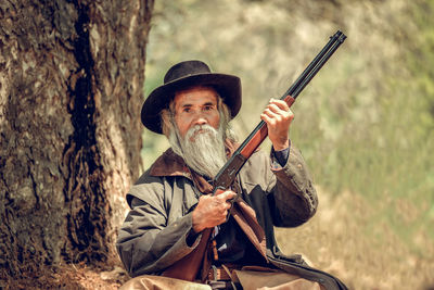 Portrait of man holding shotgun against trees