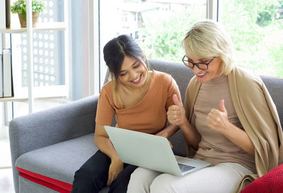 Young woman using phone while sitting on laptop