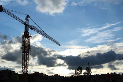 Low angle view of silhouette crane against sky in city