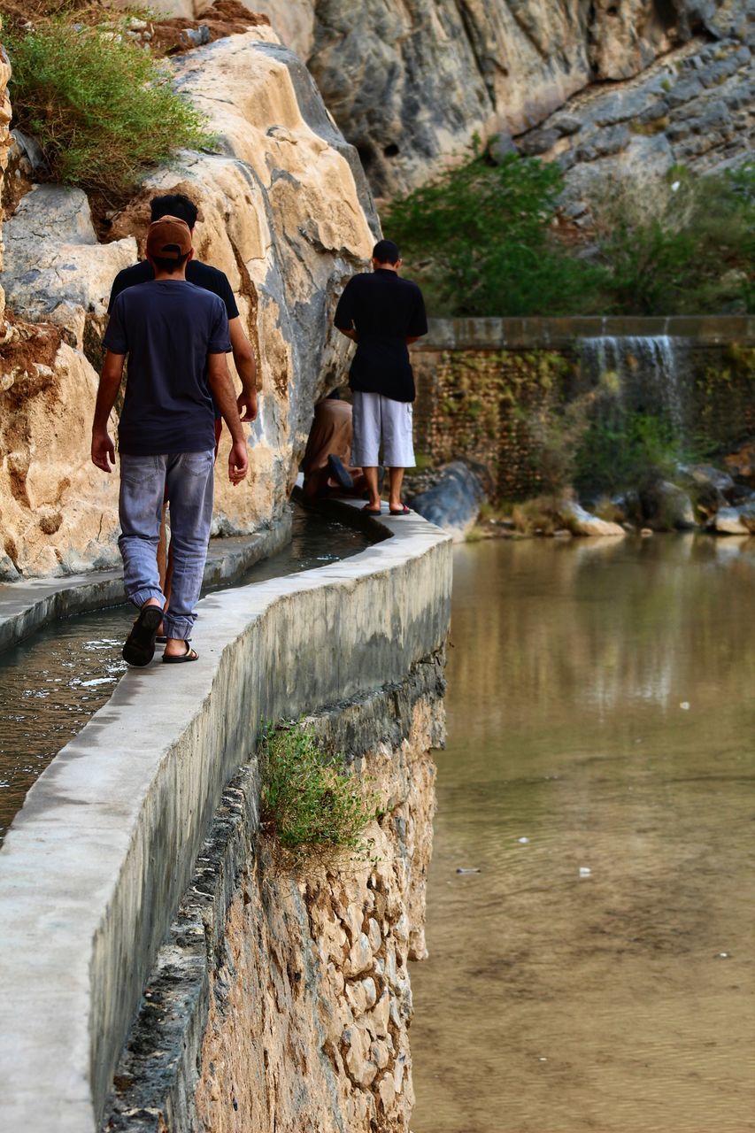 REAR VIEW OF PEOPLE WALKING ON ROCKS