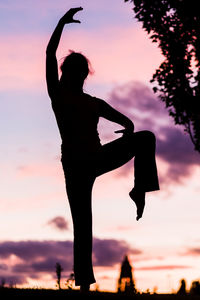 Silhouette woman with arms raised standing against sky during sunset