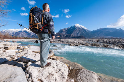 Rear view of man standing on snowcapped mountain against sky