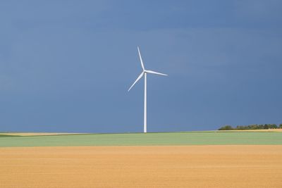 Wind turbines on field against blue sky