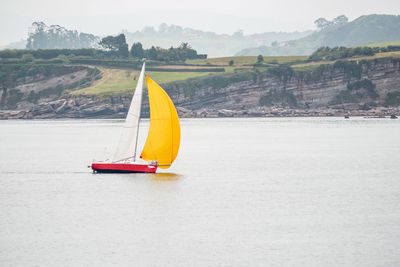 Sailboat sailing on sea against mountain