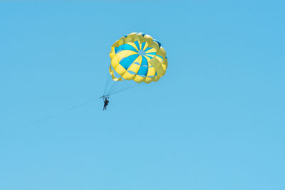 Low angle view of people paragliding against clear blue sky