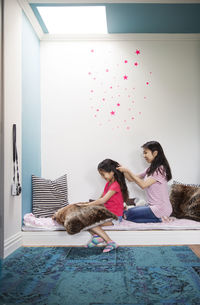 Teenage girl tying hair of sister on sofa at home