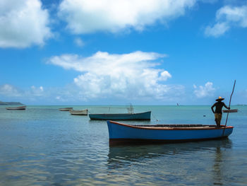 Man standing in boat moored on sea against sky