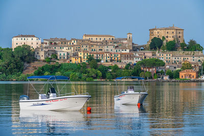 Sailboats moored on sea by buildings against clear sky