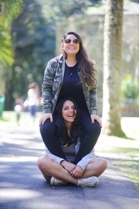 Portrait of smiling young woman piggybacking friend while sitting on footpath