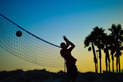 Silhouette man playing volleyball against sky during sunset