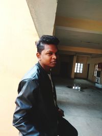 Young man looking away while standing against wall