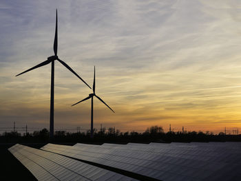 Wind turbines on field against sky during sunset