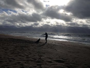 Silhouette boy standing on beach against sky