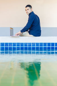 Portrait of young man sitting against wall