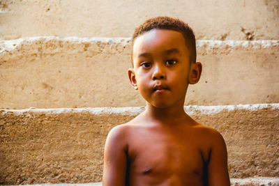 Portrait of shirtless boy standing against wall