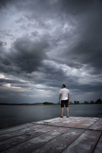 Rear view of man standing on shore against sky