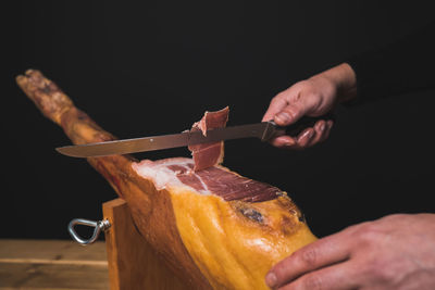 Closeup of chef cutting spanish ham with knife with black background