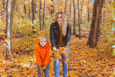 Portrait of smiling mother and son holding leaves in forest during autumn
