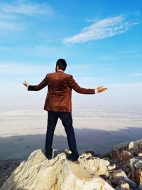 Rear view of man standing with arms outstretched on cliff against landscape