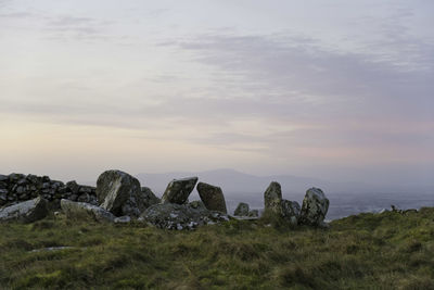 Rocks on field against sky during sunset