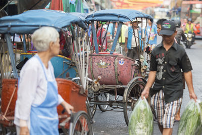 People walking by jinrikishas on street in city