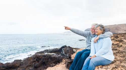 Smiling woman with man pointing by sea against sky