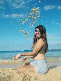 Side view of young woman sitting at beach and playing with the sand.