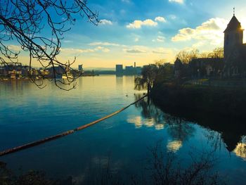 Scenic view of river by buildings against sky at sunset