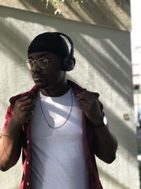 Young man wearing headphones while standing against wall