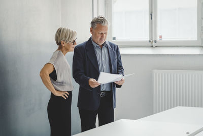 Mature businessman reading documents while discussing with female colleague in new office