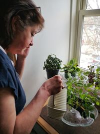 Woman watering potted plant on window sill at home
