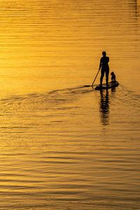 Silhouette people in sea against sky during sunset