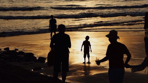 Silhouette people standing on beach against sky during sunset